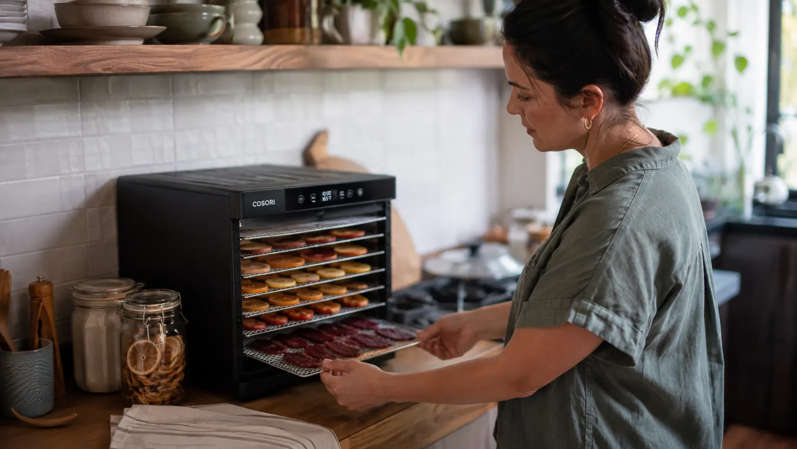 Cosori Food Dehydrator sitting on a kitchen counter with trays of sliced fruit and jerky strips loaded and ready to run