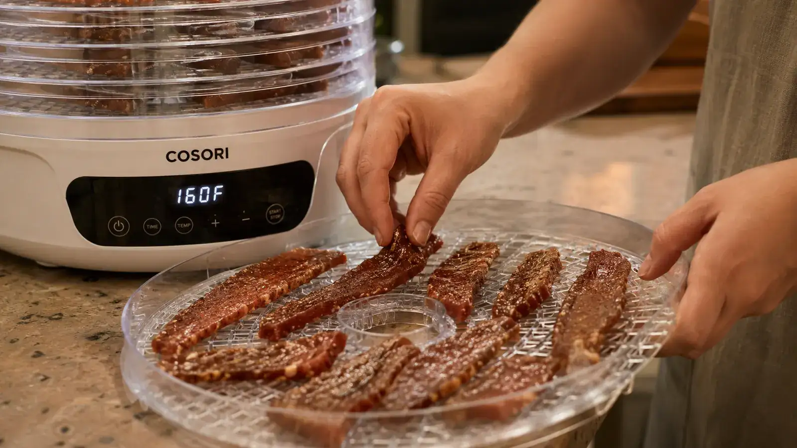 Hand loading marinated beef strips onto a Cosori dehydrator tray before starting the jerky cycle