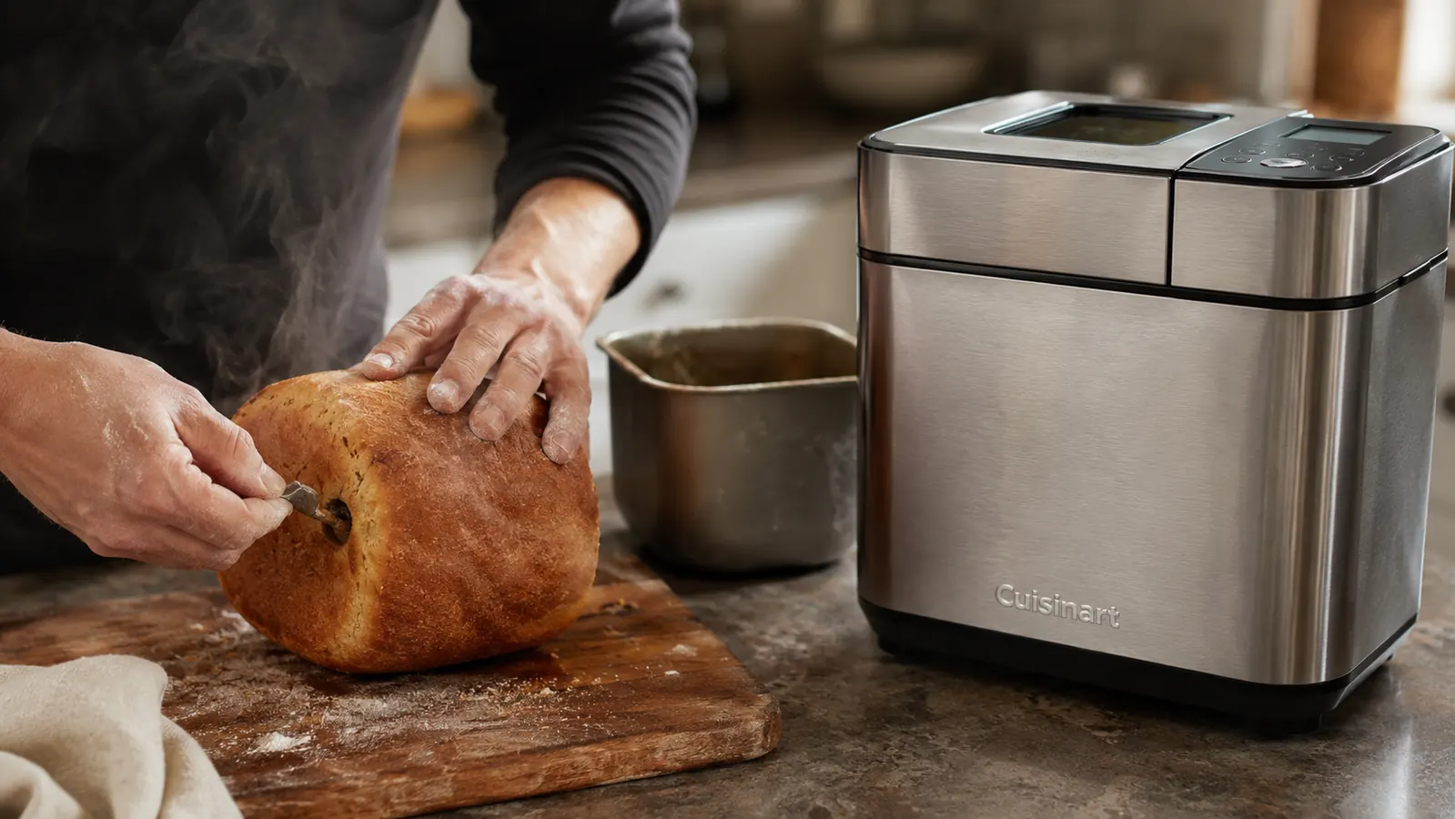 Hand pulling the kneading paddle out from the bottom of a warm loaf of bread baked in the Cuisinart Bread Maker