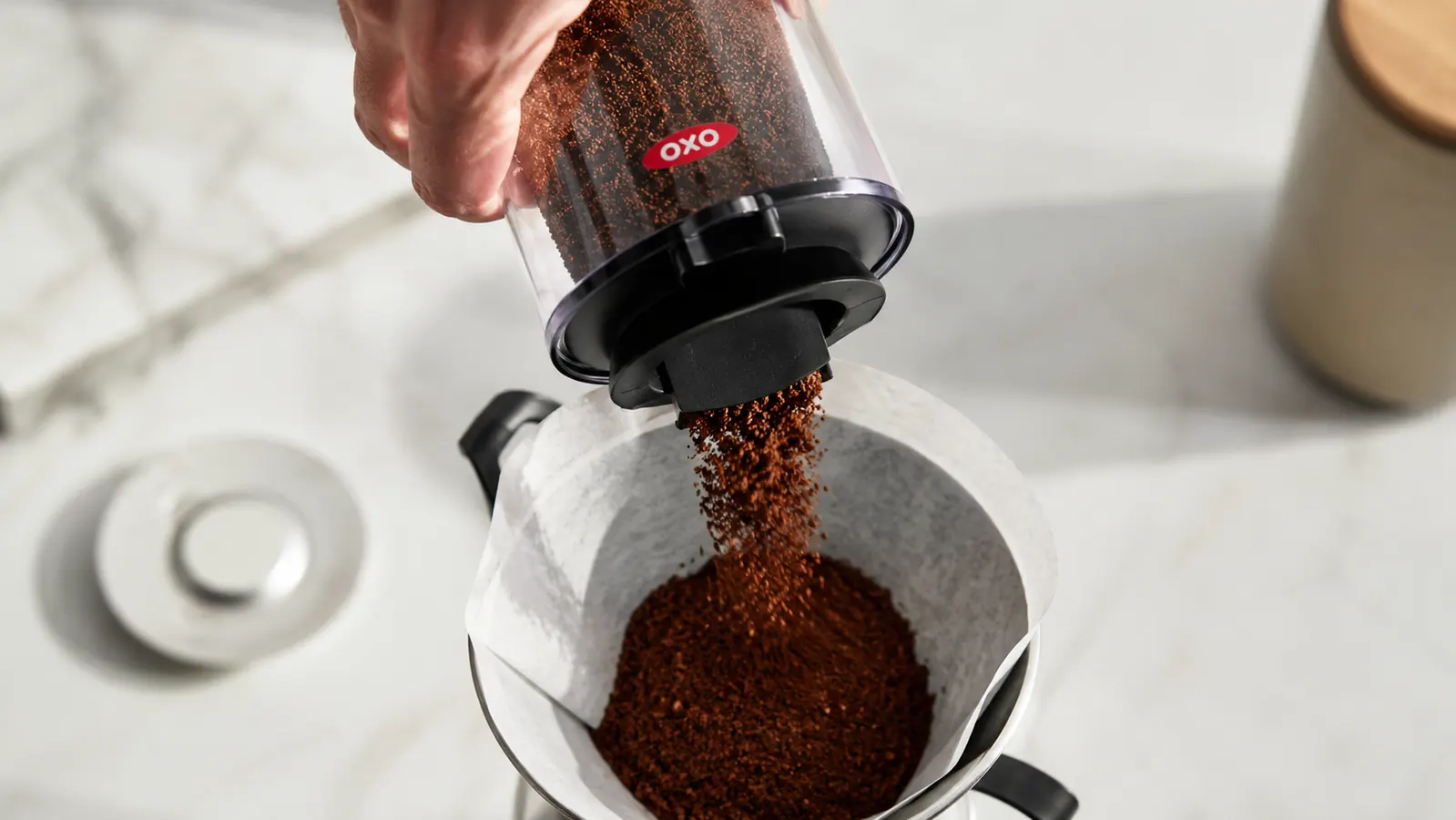 Fresh coffee grounds from the OXO Brew Conical Burr Grinder poured into a paper filter for pour-over brewing