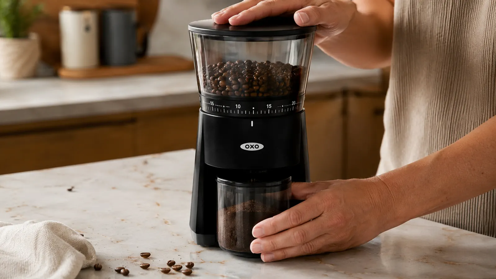 Hand pressing the one-touch button on top of the OXO burr grinder while whole coffee beans sit in the hopper