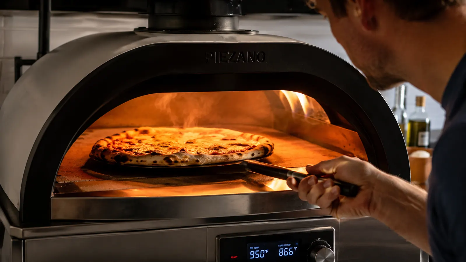 Close-up of a homemade pizza with a charred, blistered crust sitting on the ceramic stone inside a PIEZANO countertop pizza oven, steam rising